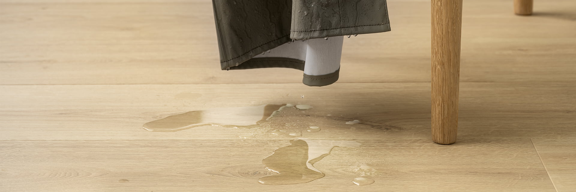 rain coat hanging on chair with water drops falling on a beige laminate floor